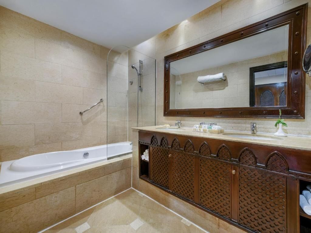 Een badkamer met een bad, een grote spiegel en een wastafel met een decor kastje.