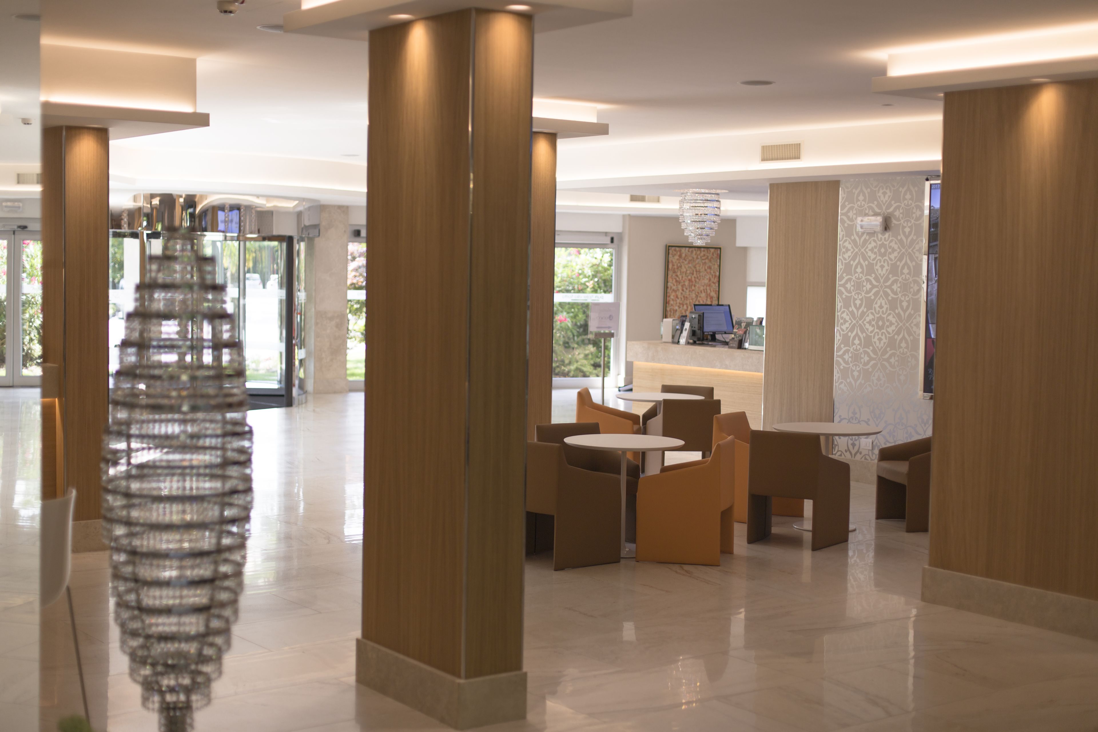 A modern hotel lobby with a reception desk, seating area, and a decorative glass sculpture.