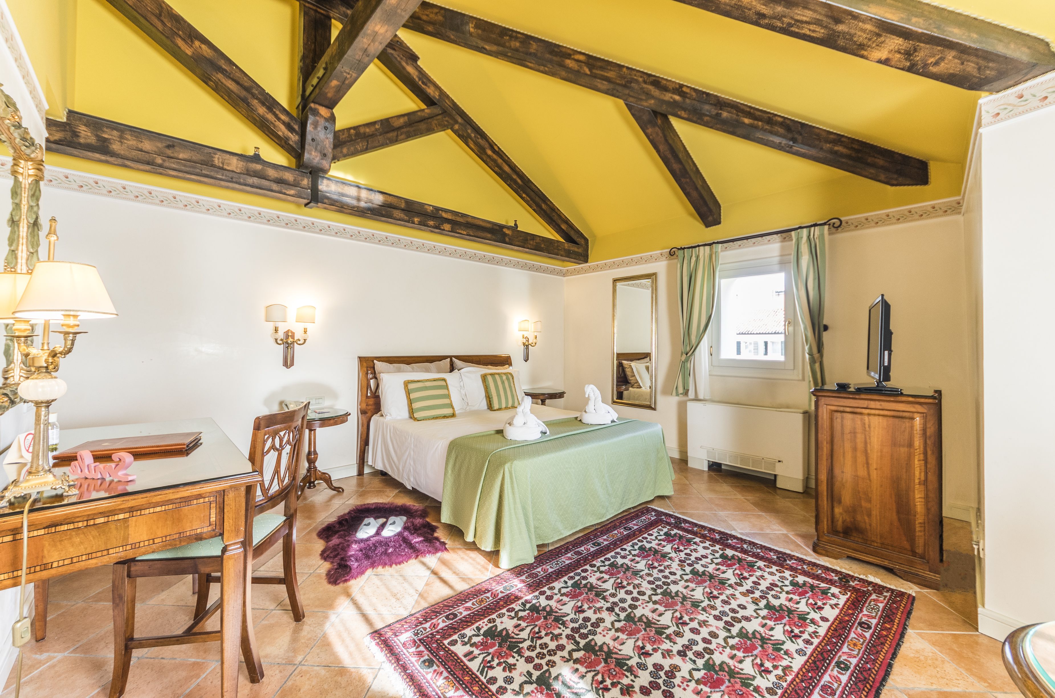 A bedroom with a bed, a desk, a chair, a rug, and a wooden cabinet.
