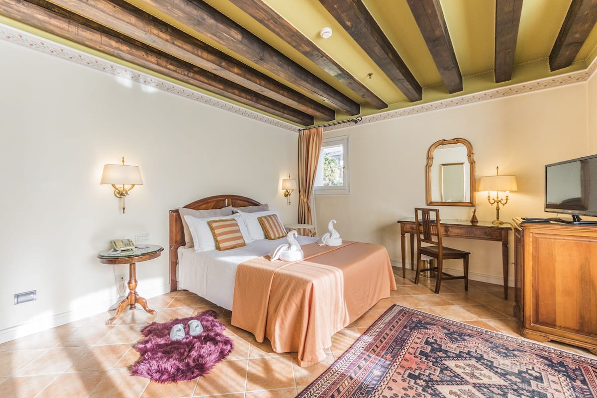 Une chambre à coucher comprenant un lit, des lampes de chevet, un bureau avec une chaise, une télévision et une fenêtre avec des rideaux.
