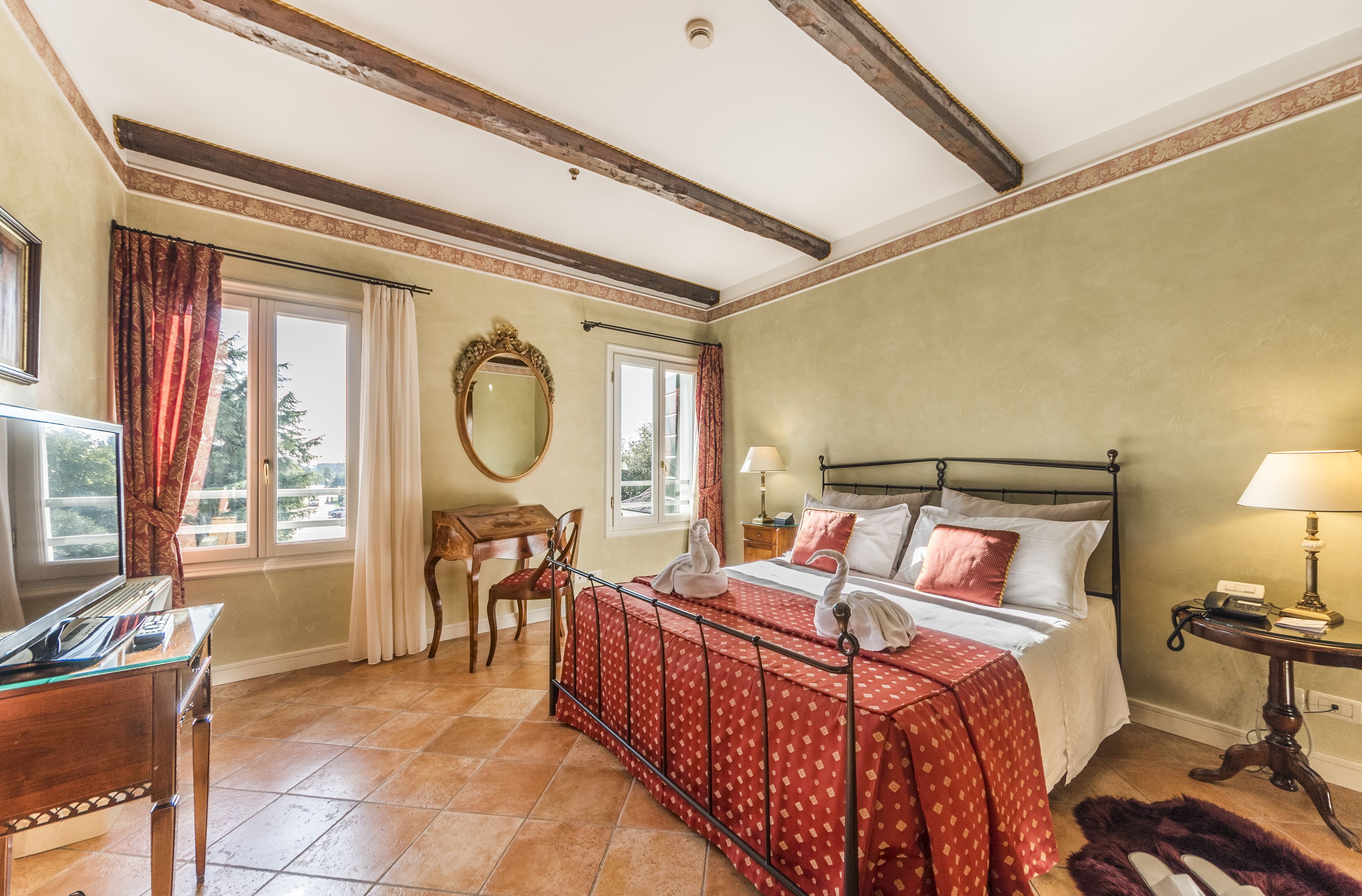 A bedroom with a bed, a desk, a chair, a mirror, and a window.
