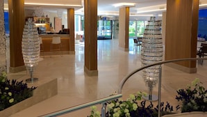 En moderne hotellobby med en central reception, to store lysekroner i krystal og en trappe med gelændere i metal.