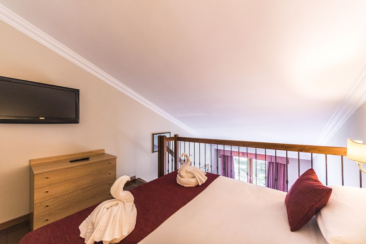 Une chambre d’hôtel comprenant un lit, une commode en bois, un téléviseur à écran plat fixé au mur et un balcon avec une balustrade.
