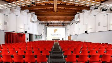 Un ampio auditorium con sedie rosse, un palco con uno schermo di proiezione che mostra 'Sogedin Hotels' e una struttura a soffitto in legno.