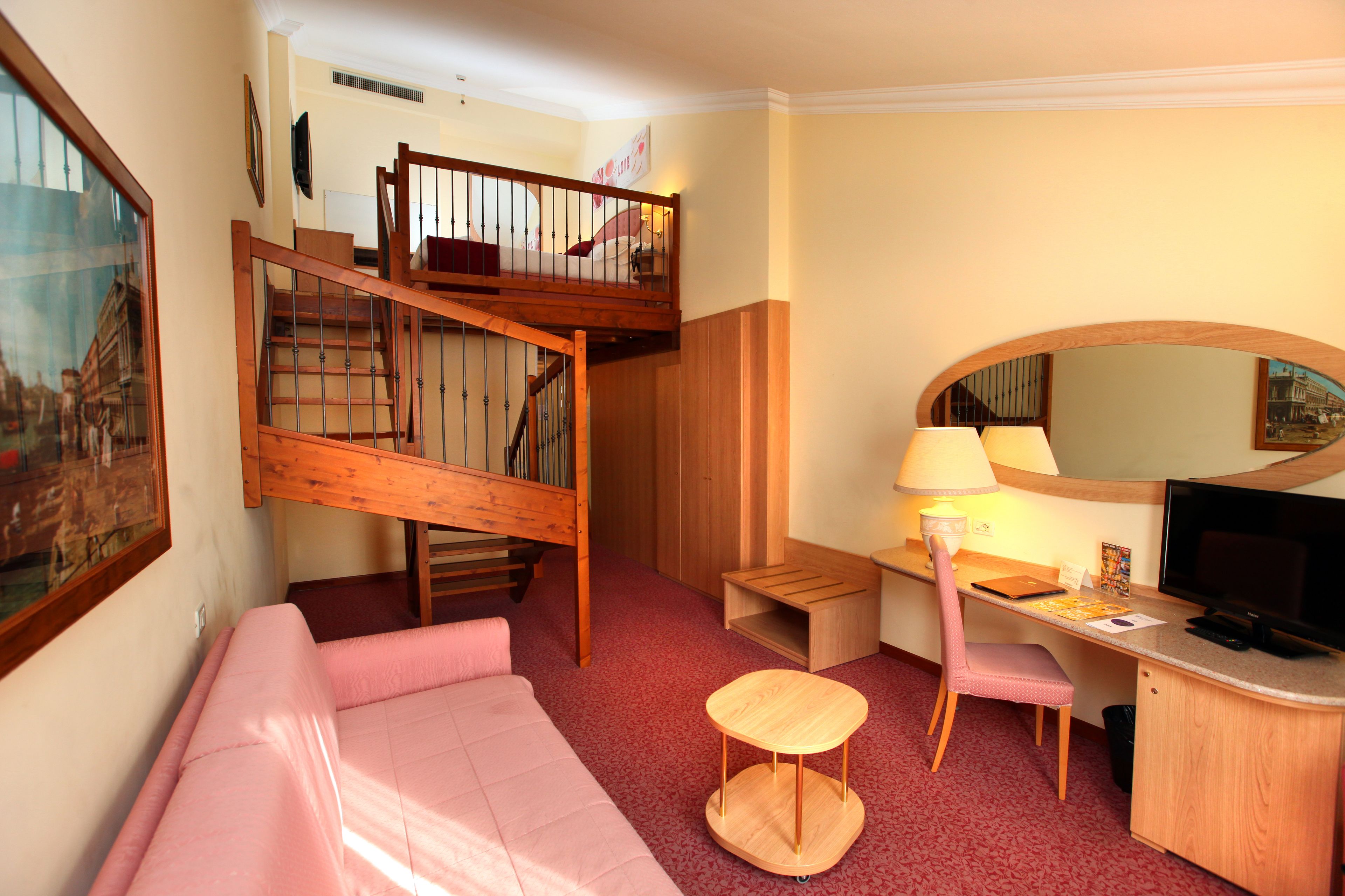 A compact hotel room with a bunk bed, a desk with a chair, a small round table, a television, and a mirror.