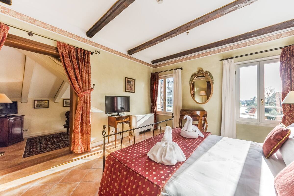 Une chambre d’hôtel avec un lit, une télévision, un miroir et une fenêtre avec des rideaux.