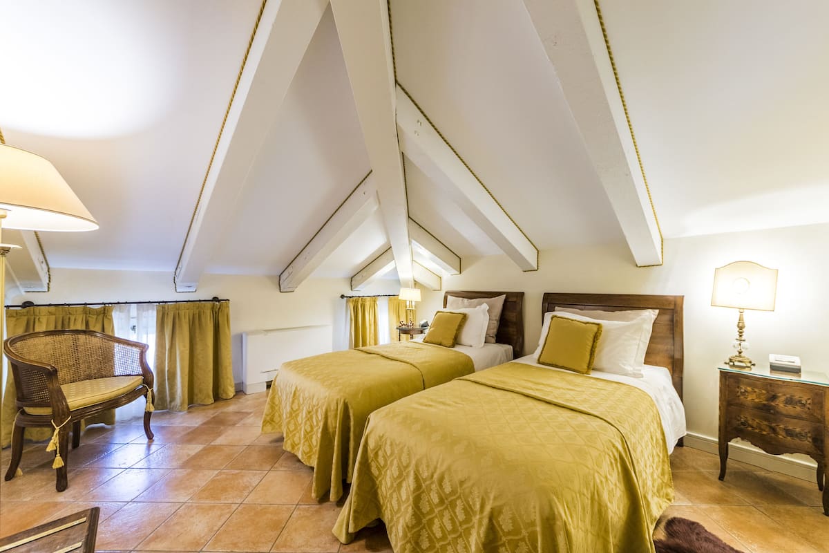 Une chambre d’hôtel avec deux lits, une chaise en bois, une table de chevet et une lampe.