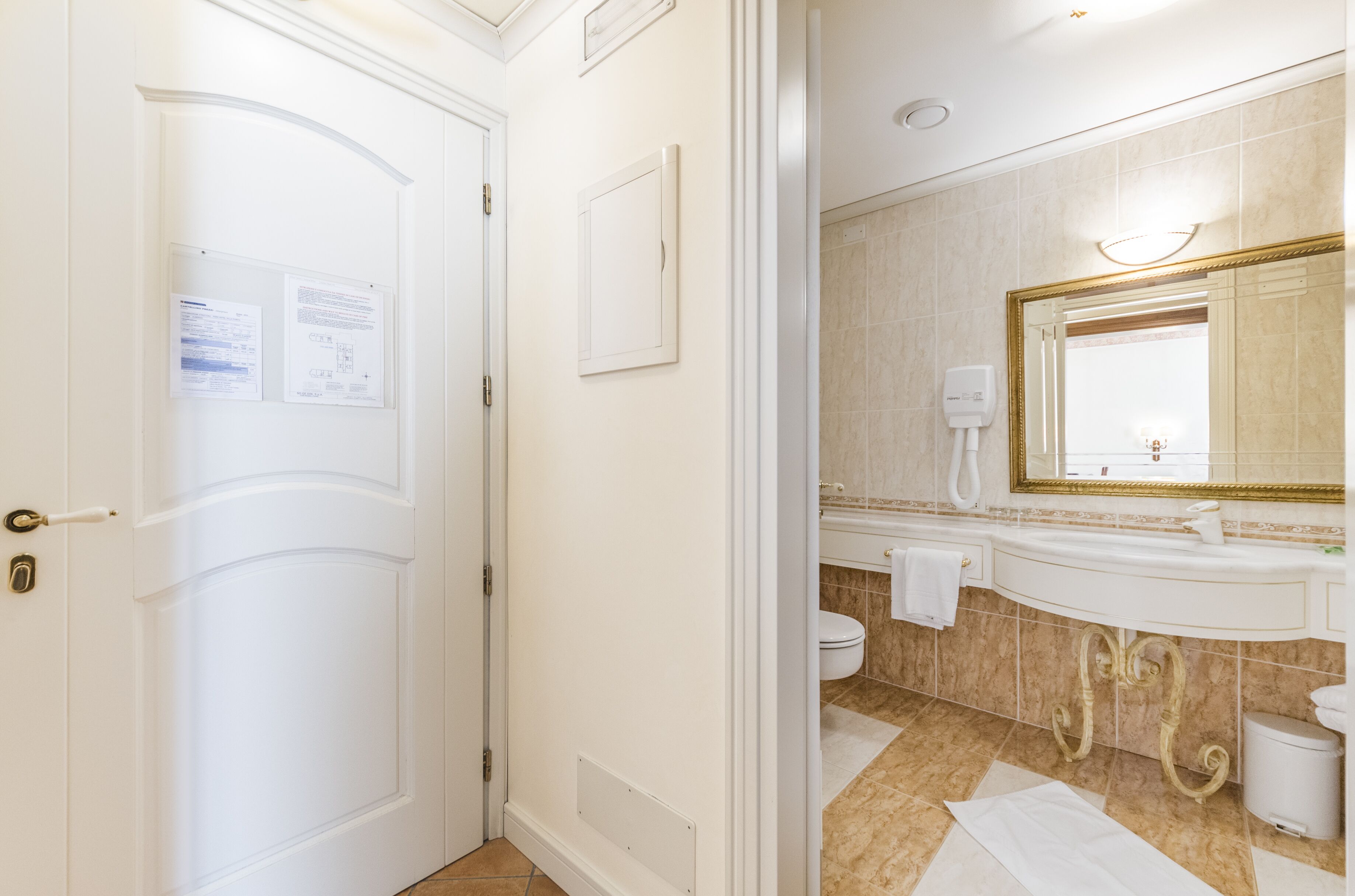 Un bagno d'albergo con una porta bianca, un lavandino con uno specchio e un water.