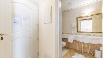 Un bagno d'albergo con una porta bianca, un lavandino con uno specchio e un water.