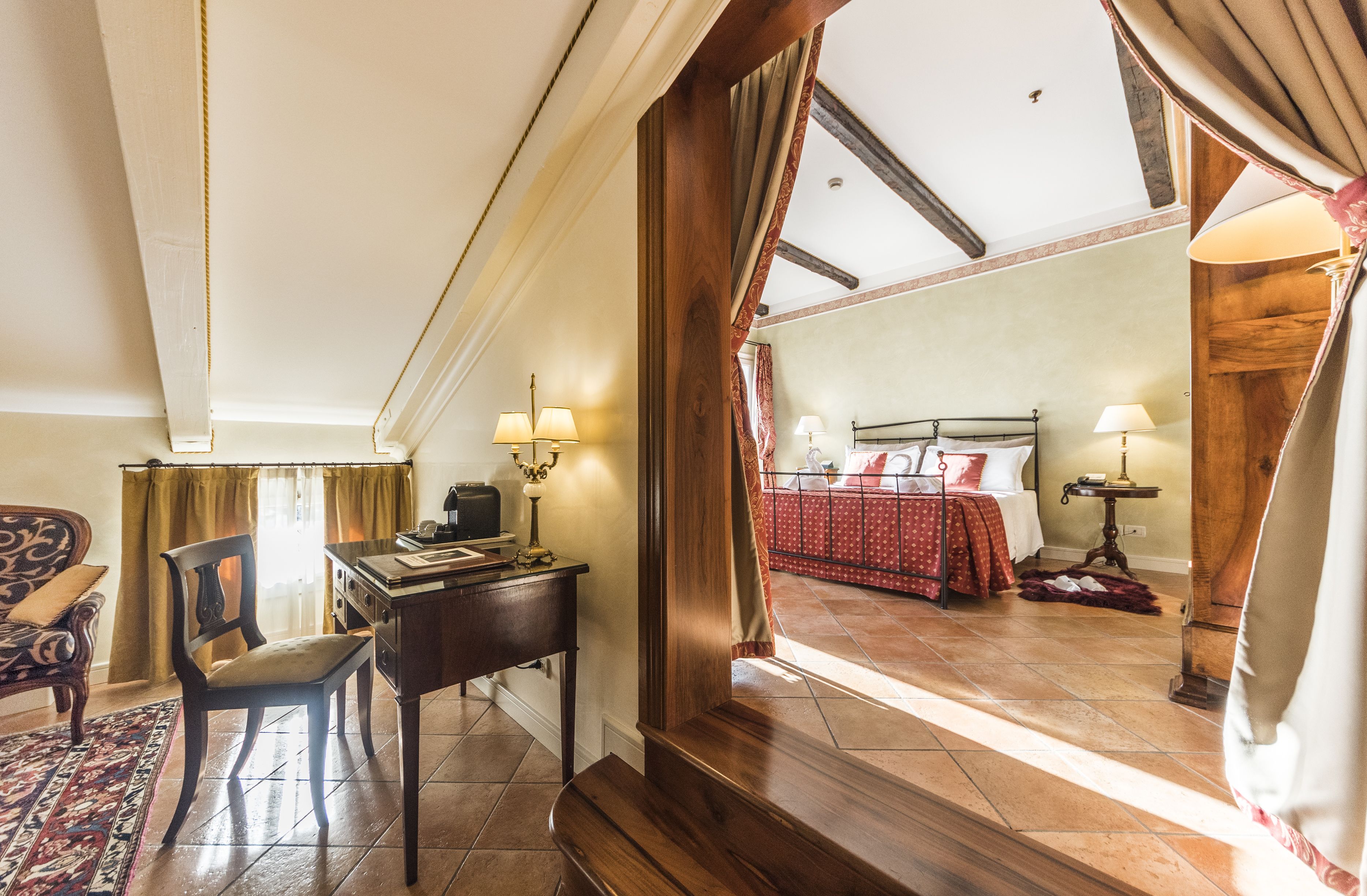 A hotel room with a wooden desk, chair, and a view of the bedroom through a doorway.