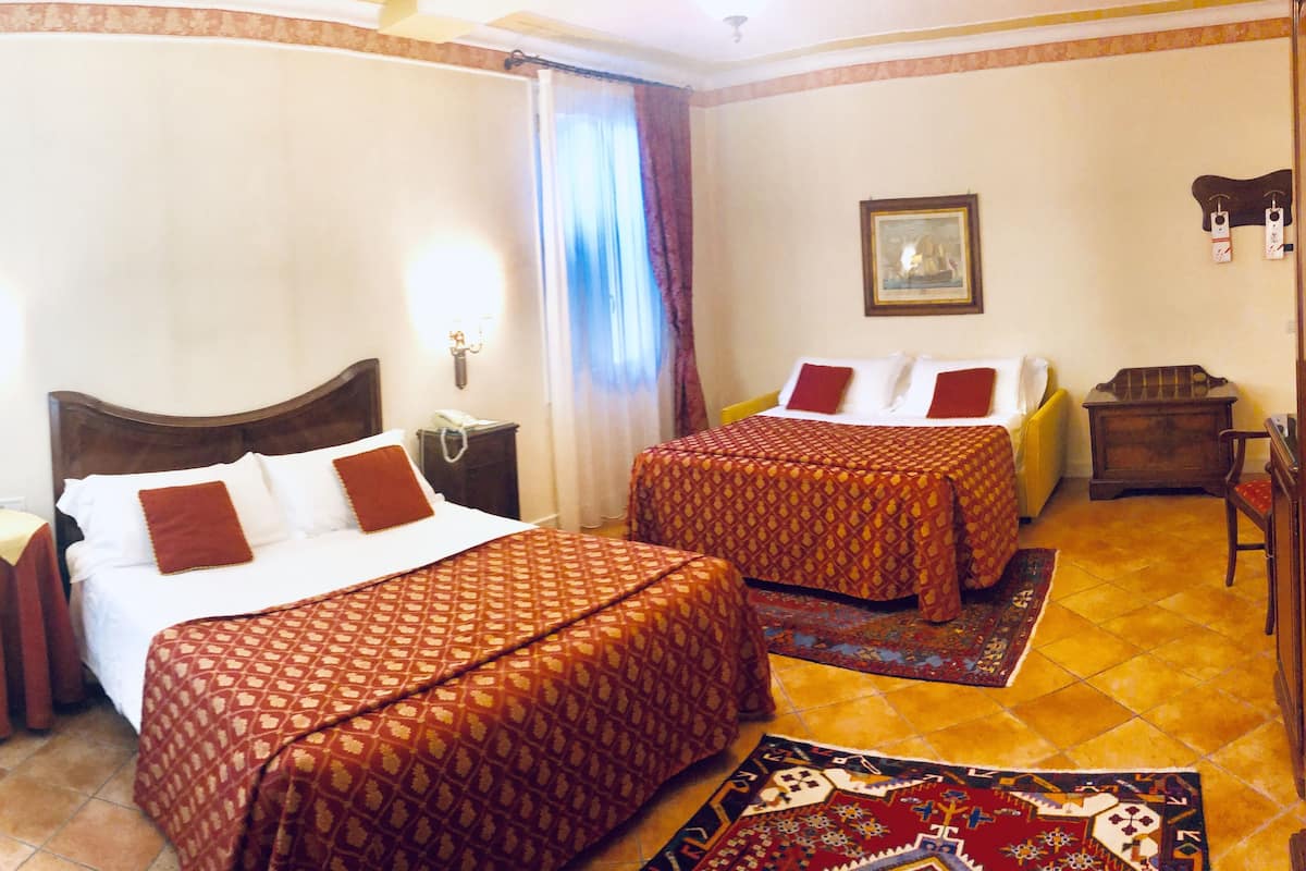 Une chambre d’hôtel avec deux lits, une chaise en bois, une petite table, un téléphone et un tableau au mur.