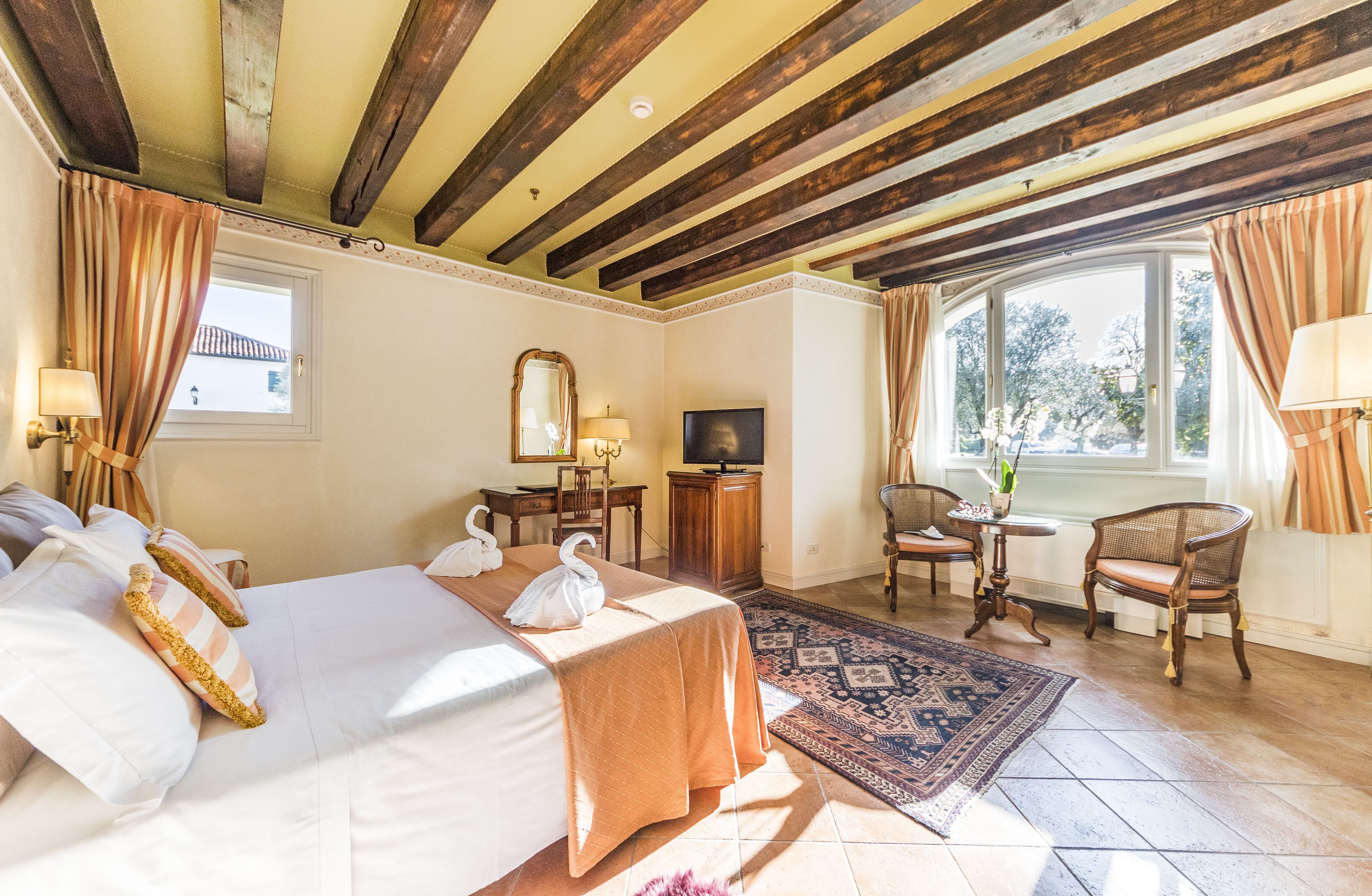 Una habitación de hotel con cama, dos sillas, una mesita, televisor y ventana con cortinas.