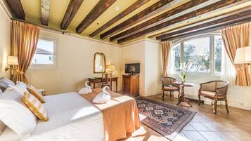 Una habitación de hotel con cama, dos sillas, una mesita, televisor y ventana con cortinas.