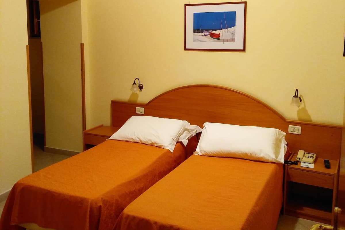 A hotel room with two beds, a framed picture on the wall, a telephone on the nightstand, and a key on the floor.