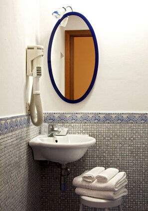 A bathroom with a white sink, a mirror with a blue frame, a towel rack with folded towels, and a wall-mounted hair dryer. - Hotel del Corso (Sorrento)