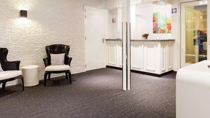 A modern hotel lobby with a white brick wall, a reception desk, and seating area with two chairs.