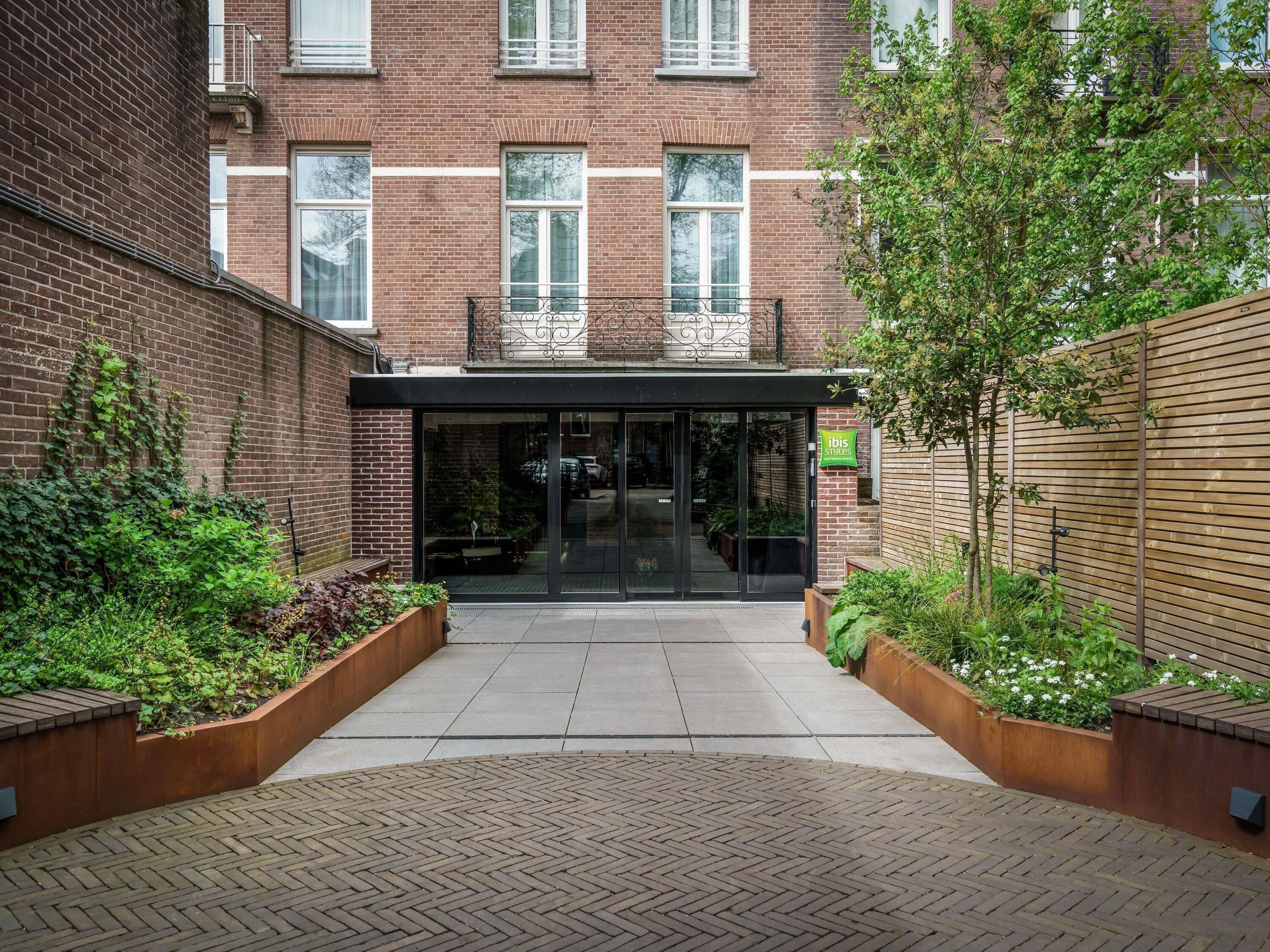 A brick building with a glass entrance, a wooden fence, and a small garden area.