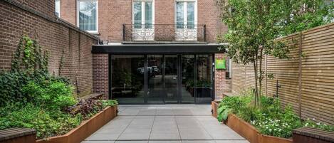 A brick building with a glass entrance, a wooden fence, and a small garden area.