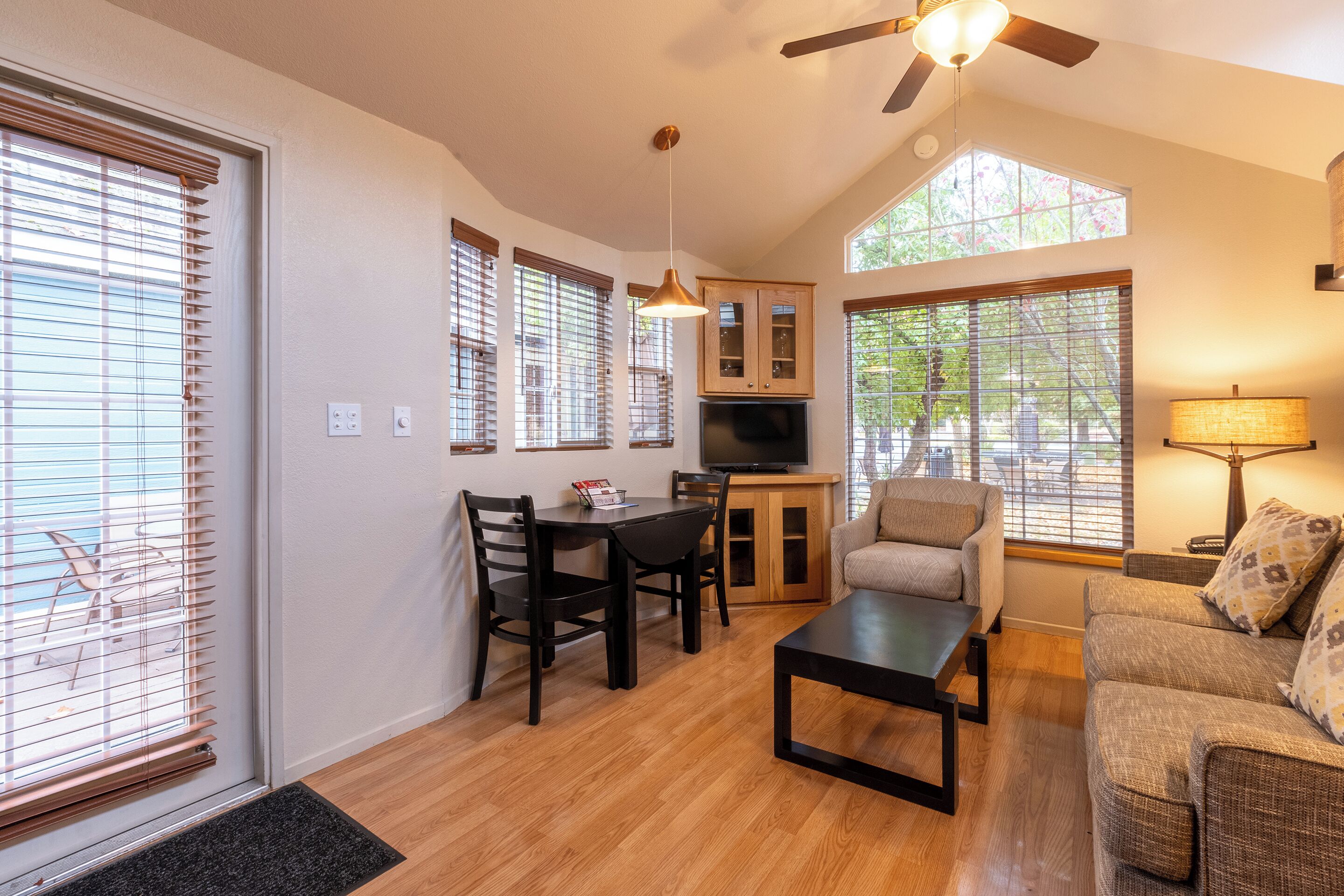 A spacious living room with a dining area, large windows, and a ceiling fan.