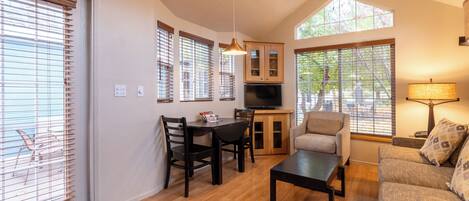 A spacious living room with a dining area, large windows, and a ceiling fan.