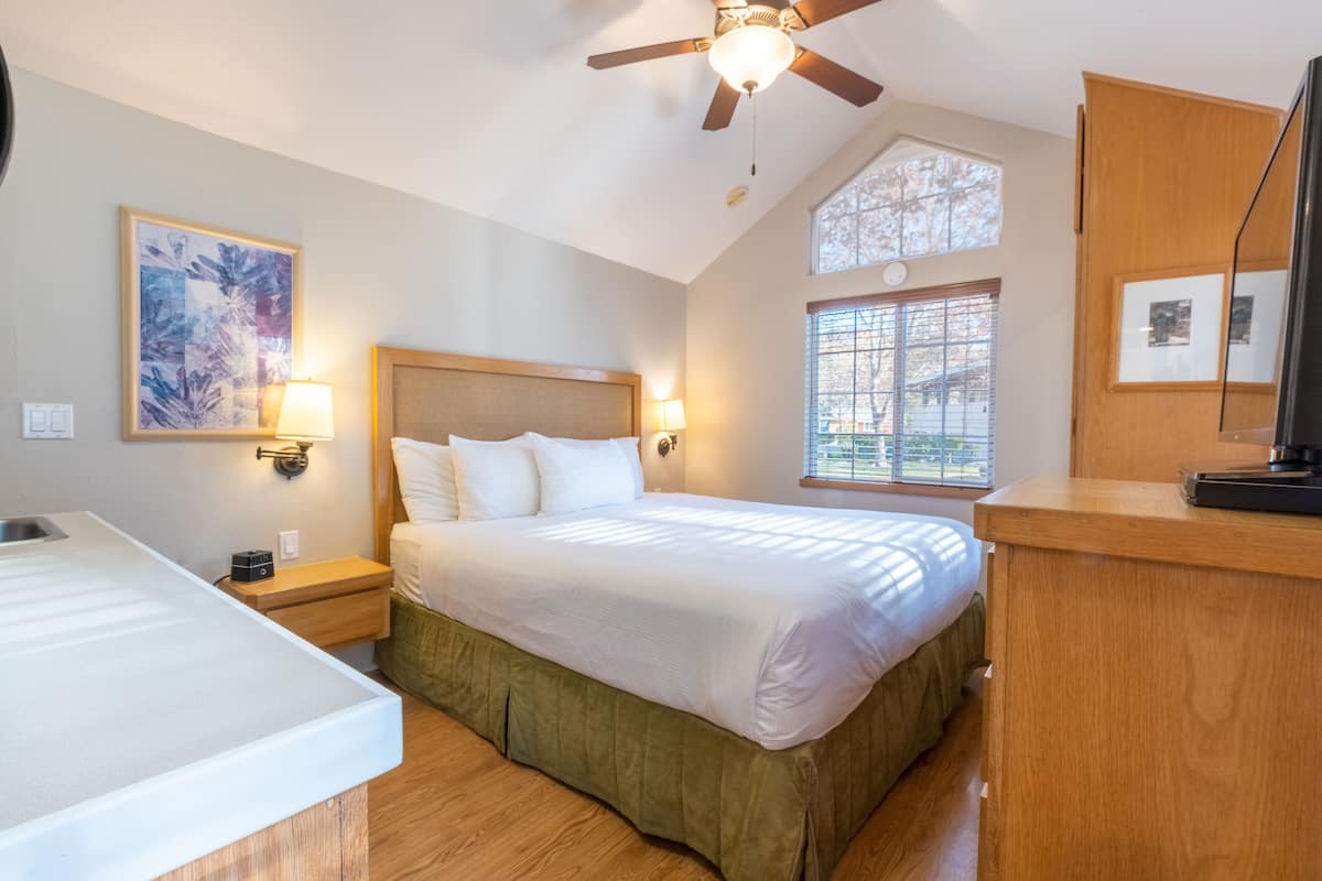 Une chambre à coucher avec un lit, des lampes de chevet, un ventilateur de plafond, une fenêtre et une commode en bois.