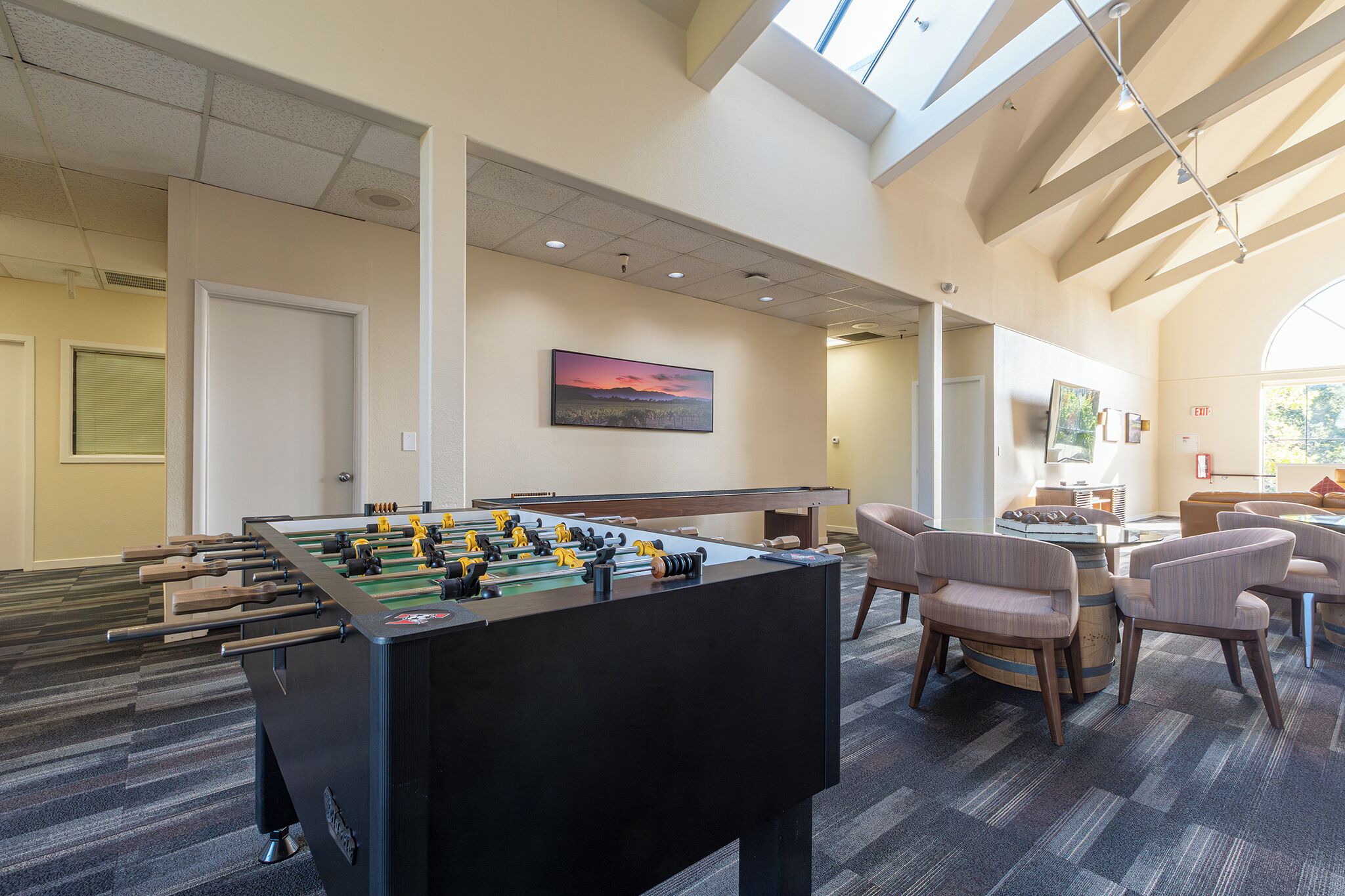 A spacious room with a foosball table, comfortable seating, and a large window providing natural light.