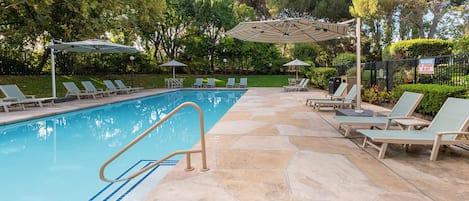 Piscina com cadeiras de sol e guarda-sóis, cercada por árvores.