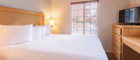 Une chambre d’hôtel avec un grand lit, un téléviseur posé sur une commode en bois et une fenêtre équipée de stores.