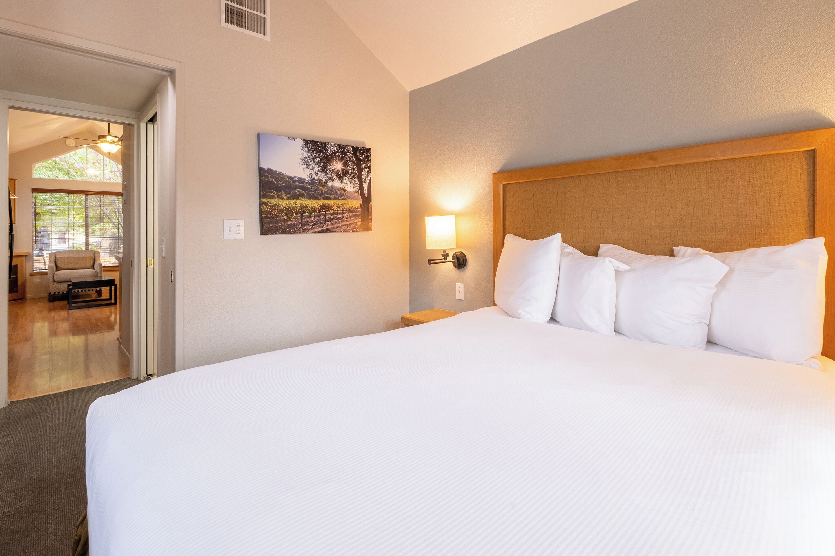 A hotel room with a large bed, a headboard, a bedside lamp, and a picture on the wall.