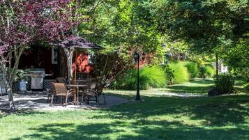 An outdoor patio with a dining table and chairs, surrounded by lush greenery and flowering trees.