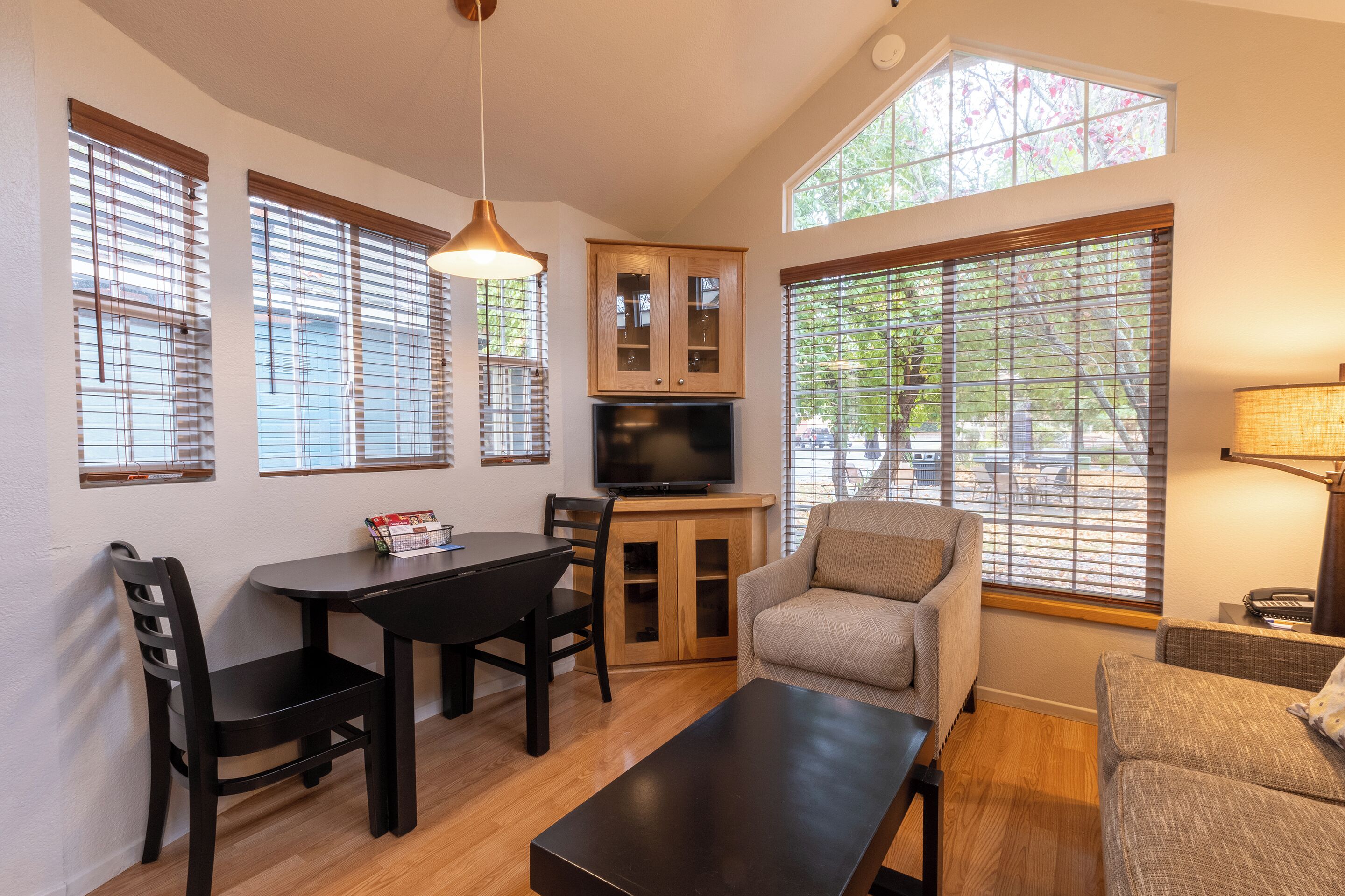 A compact living space with a dining area, a sofa, a TV, and large windows with blinds.