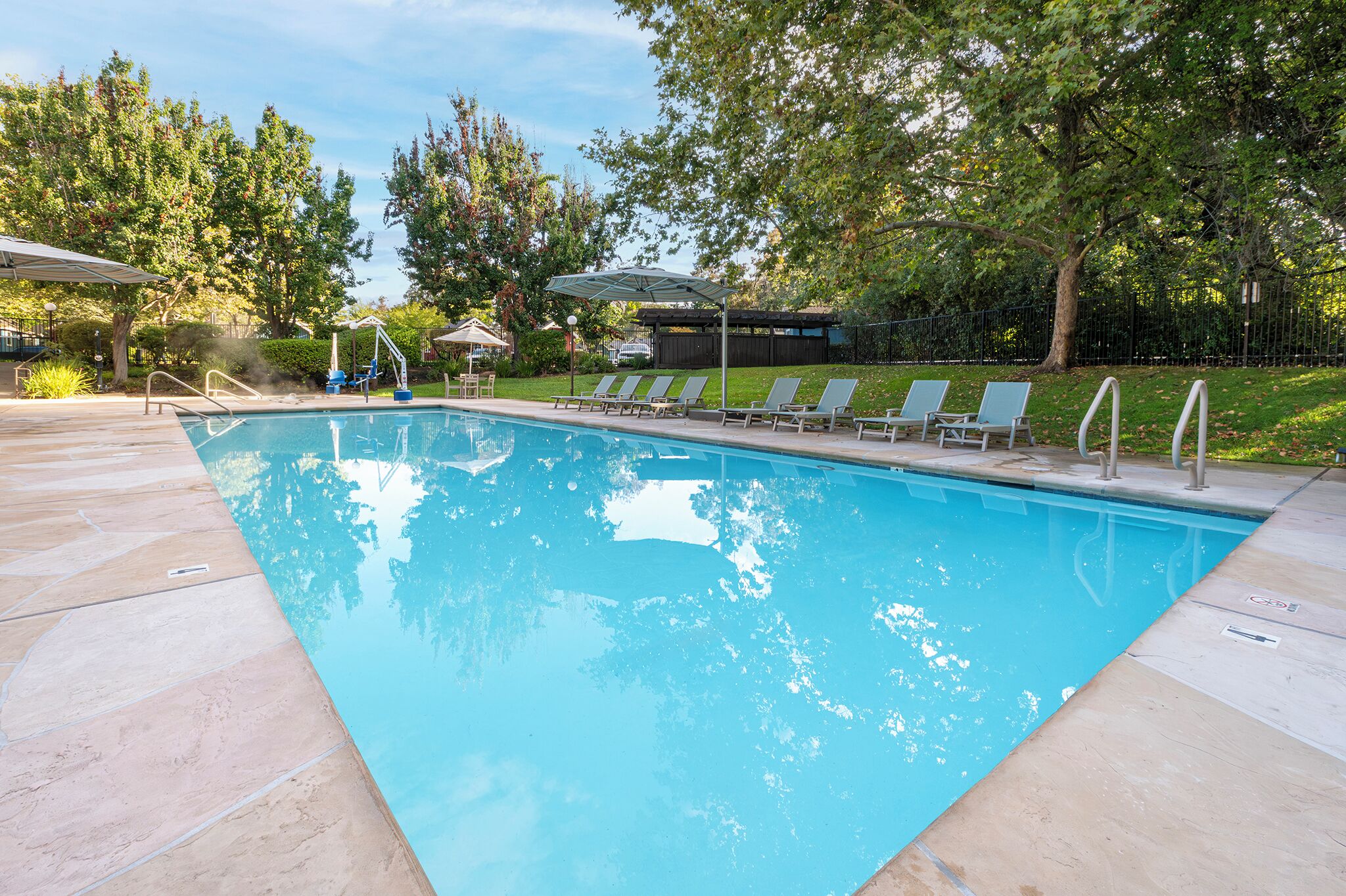 Una piscina rectangular con una cubierta de madera alrededor, equipada con una escalera y una pequeña zona cubierta para sentarse.