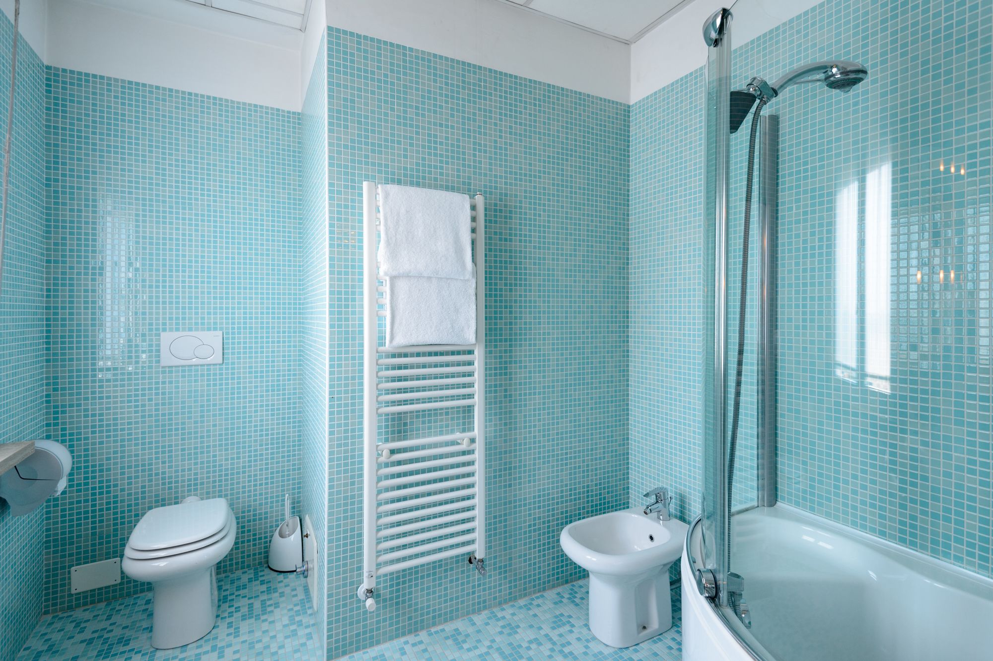 Un baño con inodoro, bidé y bañera, todo con paredes de azulejos azules.