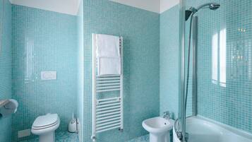 Un baño con inodoro, bidé y bañera, todo con paredes de azulejos azules.