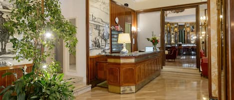 Un área de recepción con un mostrador de madera, una planta grande en maceta y un reloj fijado a la pared.