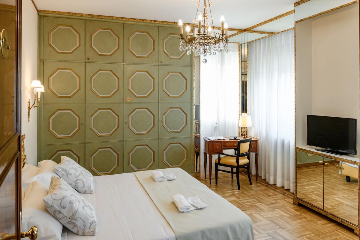 A hotel room with a large bed, a desk with a chair, a TV, and a mirror.