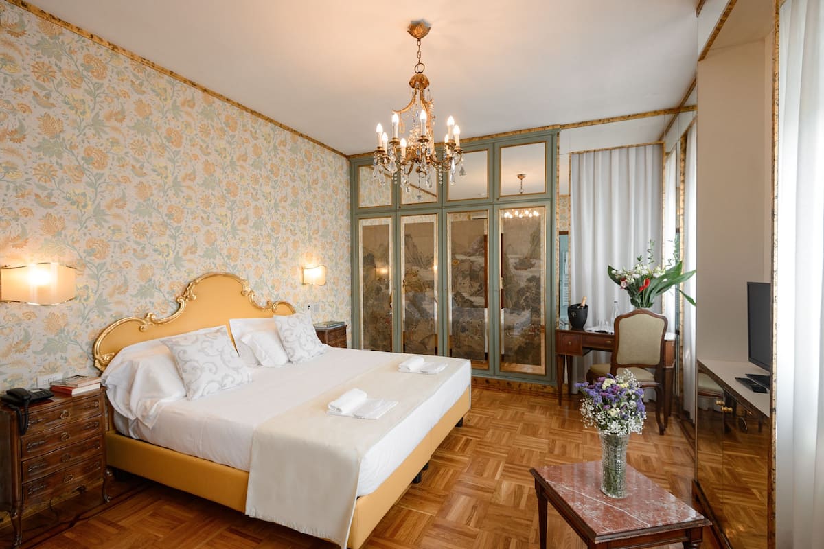 A hotel room with a large bed, a desk with a chair, a TV, and a vase with flowers.