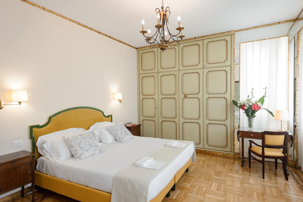A bedroom with a bed, bedside lamps, a desk with a chair, and a window with curtains.