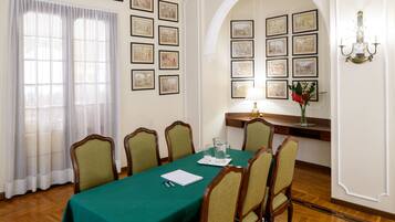 Une salle de conférence avec une table verte, six chaises, des tableaux encadrés aux murs, un bureau avec une lampe et un vase rempli de fleurs.