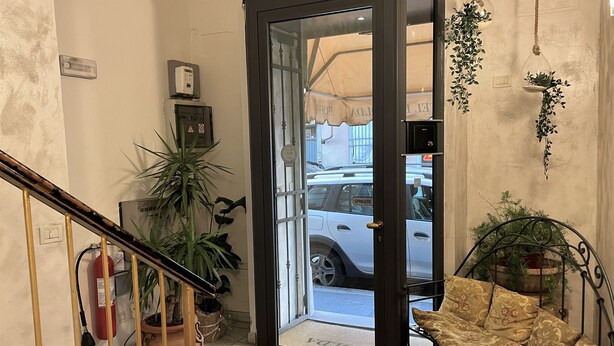 A hotel entrance with a glass door, a fire extinguisher, a potted plant, a hanging plant, and a patterned sofa. - Hotel Leopolda (Florence)