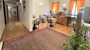 A spacious dining area with a long table and chairs, a kitchen area with a counter and appliances, and a hallway leading to a door. - Hotel Leopolda (Florence)