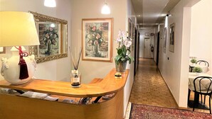 A reception area with a wooden counter, framed artwork, a vase with flowers, and a lamp. - Hotel Leopolda (Florence)