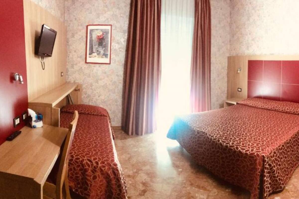 A hotel room with two beds, a desk, a TV, and a shower area.