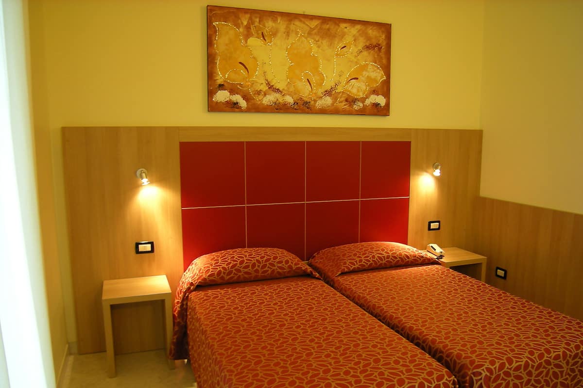 A hotel room with a red headboard, two beds, bedside tables, and a wall-mounted painting.