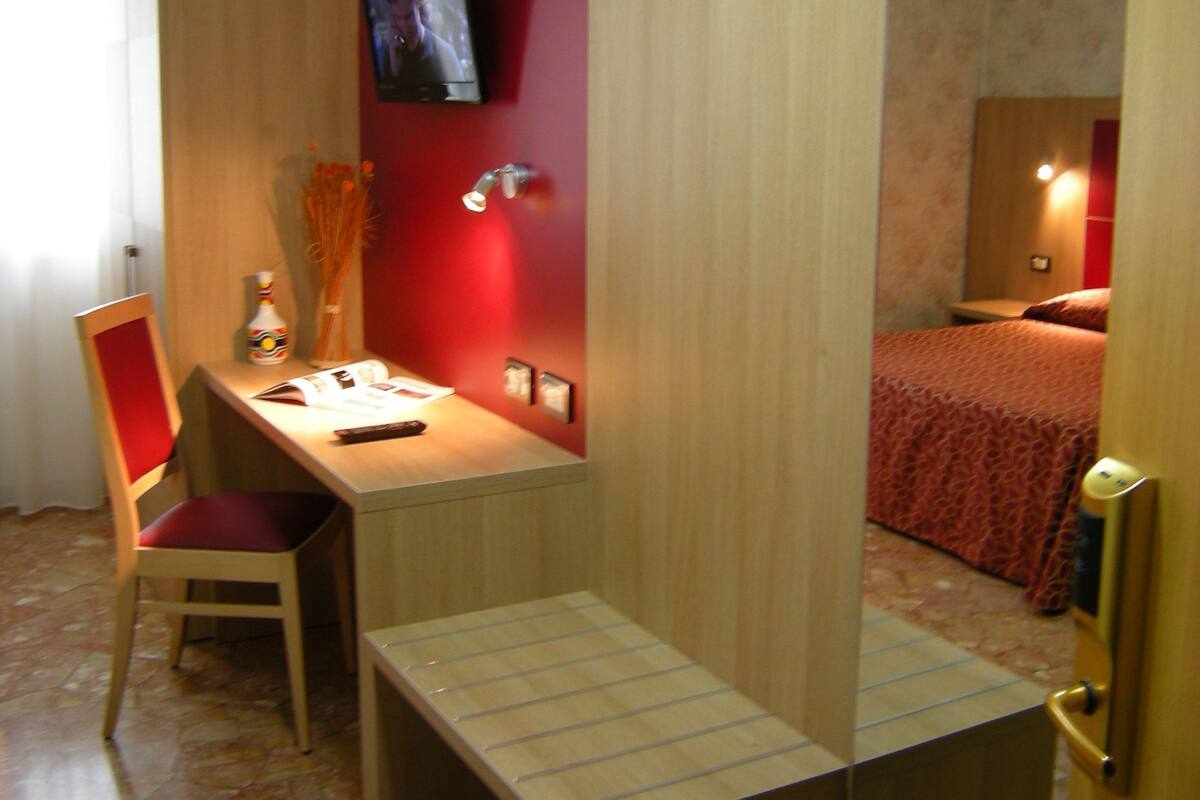 A hotel room with a desk, chair, and a television mounted on the wall.
