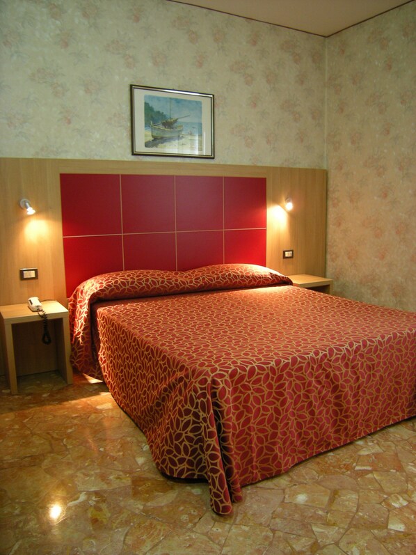 Una habitación de hotel con una cama grande, dos mesitas de noche, un teléfono y un cuadro en la pared.