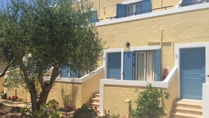 Un edificio de dos pisos con contraventanas azules, un balcón y una escalera que lleva al piso superior.