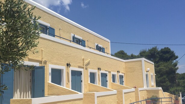 Un edificio con piscina, que presenta una escalera que lleva a un balcón con contraventanas azules y un exterior amarillo con textura.