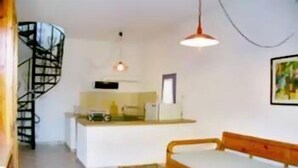 Un espacio habitable compacto con una escalera de caracol, una kitchenette, un sofá de madera y una mesa de centro de vidrio.