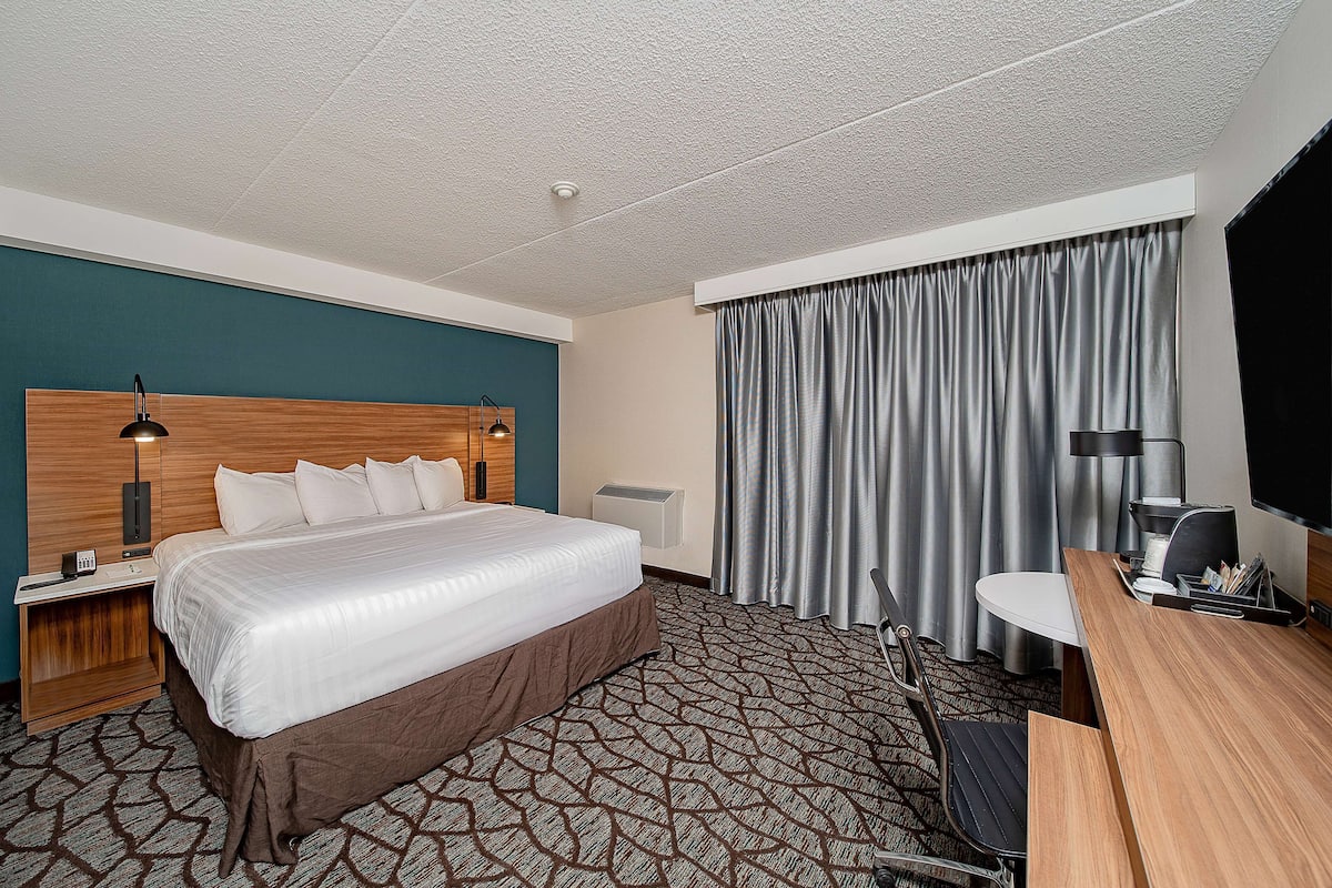 Une chambre d’hôtel avec un grand lit, un bureau, une chaise, une télévision et une fenêtre avec des rideaux.